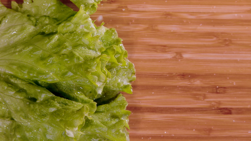 SLOW MOTION, TOP DOWN, CLOSE UP, COPY SPACE: Wet romaine lettuce leaves fall onto the empty wooden chopping board. Cinematic shot of water droplets flying as wet iceberg hits the chef's cutting board. | Shutterstock HD Video #1091919537