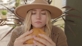 Girl enjoys delicious food at the outdoor cafe. Pretty woman eating a burger and wiping a sauce off her lips. High quality 4k footage