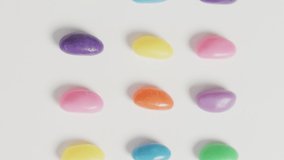 Video of overhead view of rows of multi coloured sweets over white background. fusion food and sweets concept.