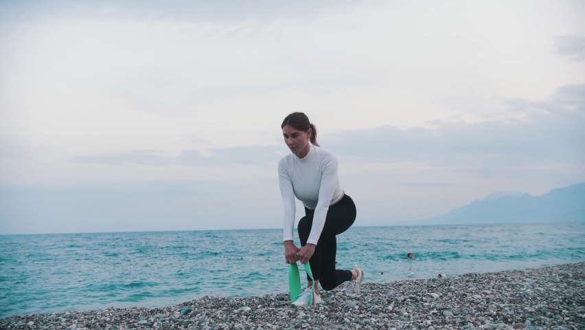A woman in white sweater doing exercises with elastic band on the pebble beach