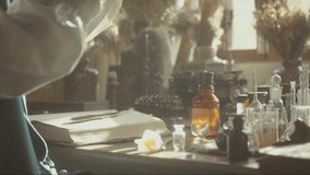 A close-up of a perfumer at his desk looking for a new fragrance. Vintage cinematic perfumery concept. Sunny day in the working workshop. Lots of ingredients, glass flasks. Depth of field. 4K video