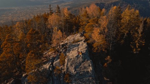 cinematic aerial footage from drone flying around couple hikers sitting on top of cliff. travelers enjoying great view in Carpathian mountains, Ukraine. happy girl and man together at sunset.