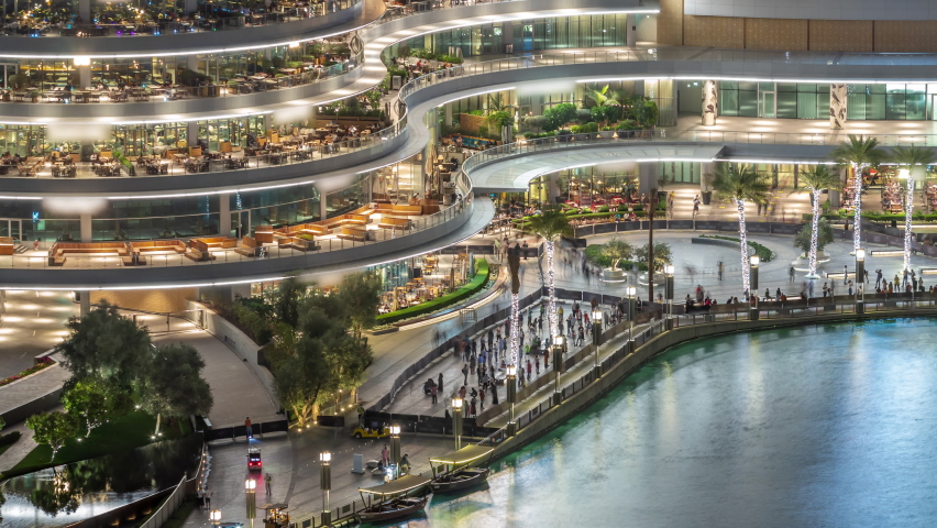 Shopping mall balcony with reataurants near fountain in Dubai downtown aerial night timelapse, United Arab Emirates. Illuminated waterfront walking area