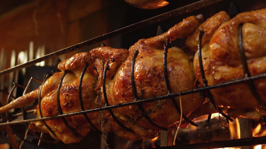 Roasted chickens on spit grilled over wood fire on big bbq barbecue with a spoon spilling sauce on it Royalty-Free Stock Footage #1091939485