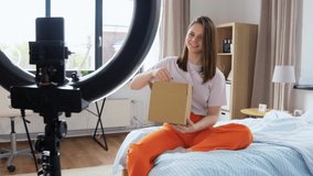 blogging, technology and people concept - happy smiling girl or beauty blogger with ring light and smartphone unpacking parcel box with cosmetics at home