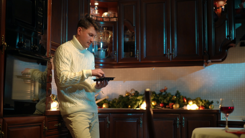 Heartbroken stressed man eating sweet candies standing in kitchen at home. Side view portrait of sad Caucasian guy chewing unhealthy junk food thinking looking away. Sadness and depression