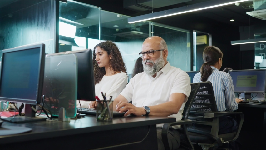 A track in shot of an elderly or old Indian Asian working man or male sitting front of the computer with office colleagues or employees looks at the camera and smiles. Healthy work environment concept | Shutterstock HD Video #1091942463