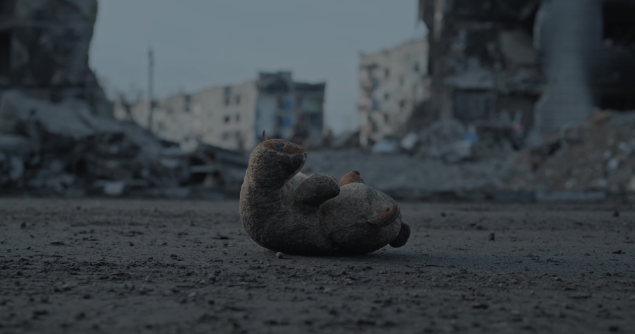 Bottom view of abandoned toy on ground in destroyed Ukrainian city. Child's teddy bear lying on background of burnt residential buildings during Russian - Ukrainian war. Invasion of territory Ukraine