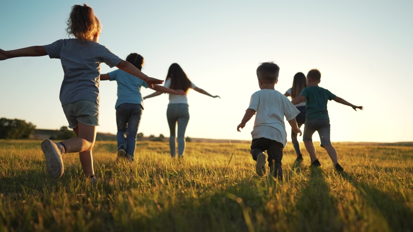 Happy holiday in nature. Family and friend run together on green grass in summer.Active children walk in the park at sunset.Child have fun play and run in spring in field.Family picnic on green grass. Royalty-Free Stock Footage #1091945921