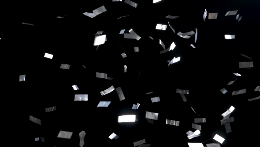 Silvery ribbons of confetti falling down on an isolated black background. Particles glitter shimmers and sparkles in studio light. Festive background for holiday, birthday, wedding, party, new year. Royalty-Free Stock Footage #1091945977