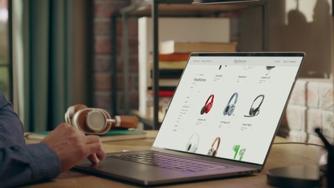 Man Using Laptop Computer, Online Shopping for Electronics, Wireless Hi-Fi Headphones. e-Commerce Concept of Purchasing, Buying, Ordering Tech Devices on Website. Over Shoulder Close-up Screen Shot