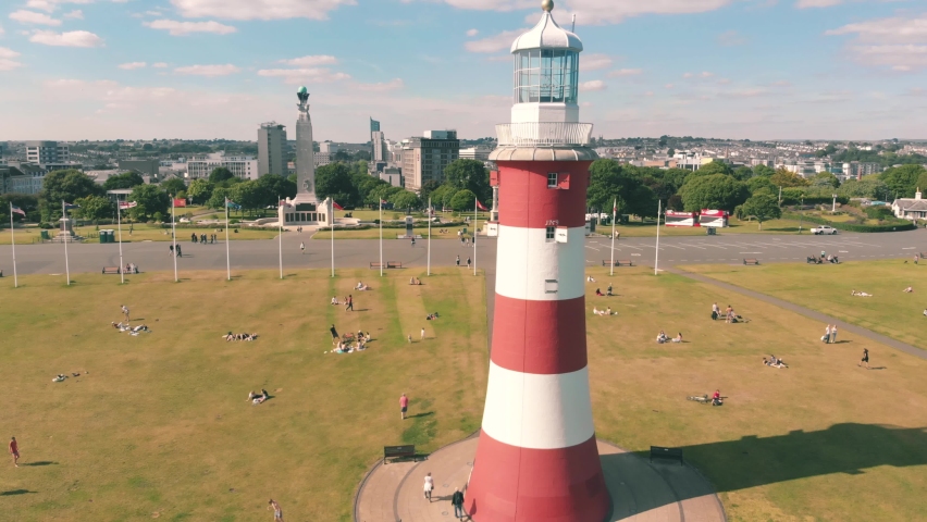 Aerial drone shot of a red and white striped lighthouse on the coast in Plymouth, UK Royalty-Free Stock Footage #1091946941