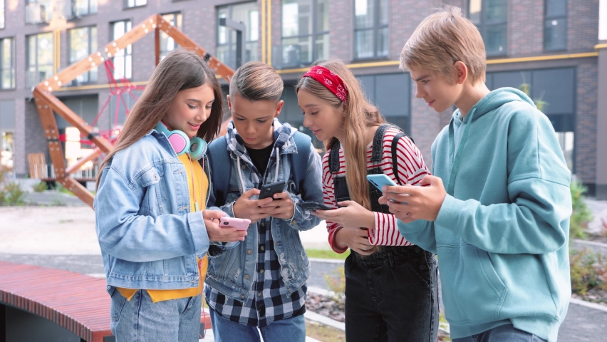 Cheerful stylish teenagers using smartphones gadgets on street in city. Happy positive teens friends texting on cellphones gadgets and talking. Friendship, technology concept. Playing game online Royalty-Free Stock Footage #1091948337