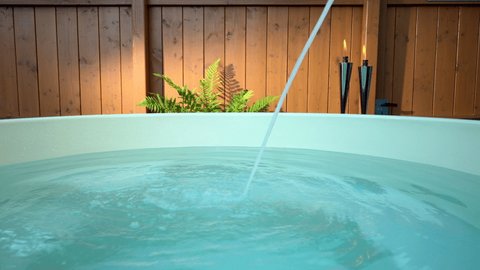 Hot tub being filled with a stream of water. Set against a backdrop of a beautiful wooden fence, a healthy green fern illuminated by a streak of sunlight and two lit chrome garden torches flickering.