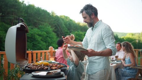Man grilling ribs and vegetable on grill during family summer garden party, close-up Video stock