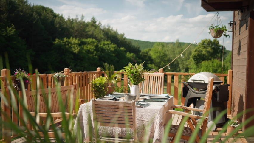 Dining table with wooden chairs set for dinner on the terrace with grill in summer, garden party. concept. | Shutterstock HD Video #1091951265