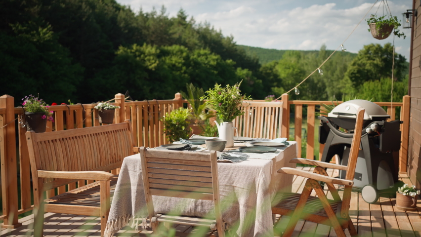 Dining table with wooden chairs set for dinner on the terrace with grill in summer, garden party. concept.