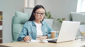 young asian girl student studying online remotely using video call remote lessons sitting at desk at home or classroom. indoor. Woman writes in notebook takes notes while looking at laptop screen