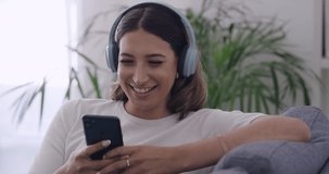 Woman laughing watching funny videos online with her phone at home. Female streaming series and chatting with friends on social media. Girl smiling while sending text message and listening to podcast