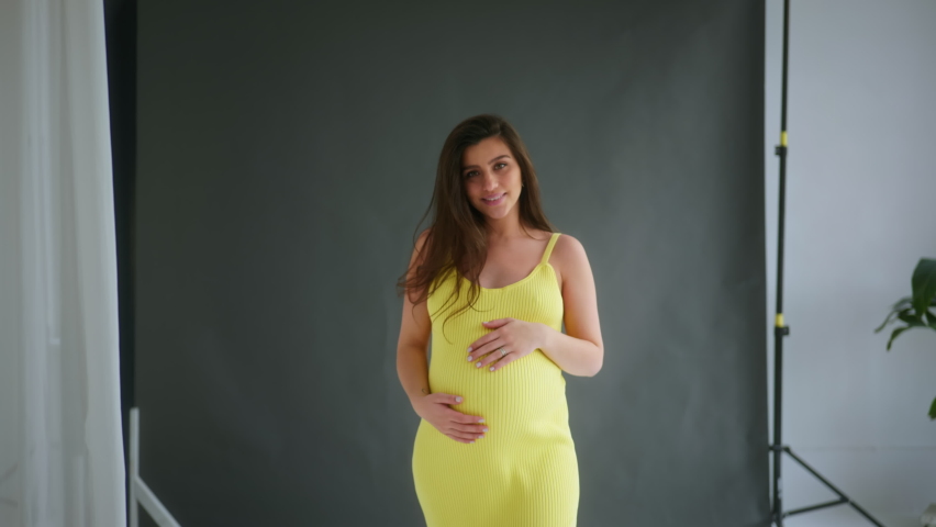 expectant mother. A young pregnant brunette girl slowly strokes her belly. A pregnant girl in her final months is running her hands over her belly. Pregnancy, last month, expectant mother. General