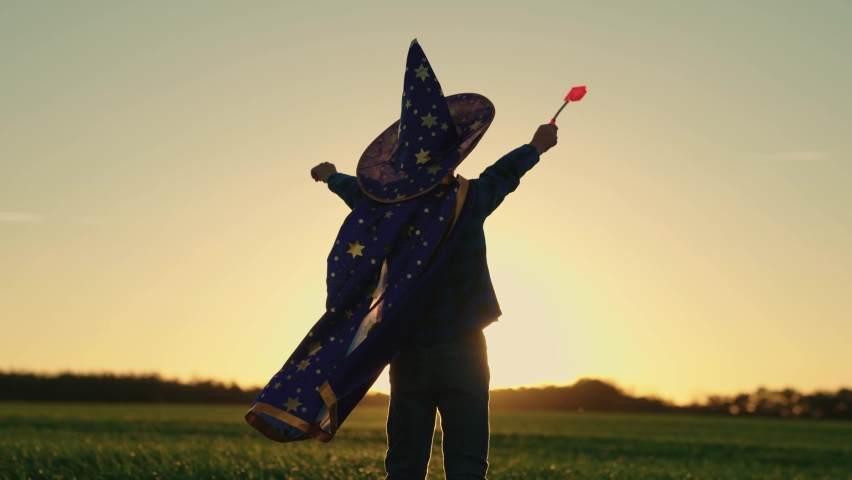 Kid in carnival costume for holiday, astronomy festival outfit, childrens dream. Child boy in wizards hat plays, conjures with magic wand in sun. Childrens dreams, halloween, childrens magic at sunset Royalty-Free Stock Footage #1091959205