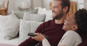 Video of happy diverse couple watching tv on sofa. Love, relationship and spending quality time together at home.