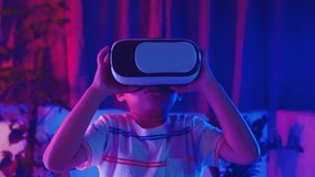 Asian little kid boy wearing virtual reality goggles experiencing reality, Child wear VR helmet look left look right and excited at home dark purple and blue background, Virtual technology