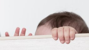 baby holding from edge of the crib with both hands and crying,try to get out of bed.cute toddler sad,unhappy to stay in wooden child crib with bars. wooden material.maternity concept