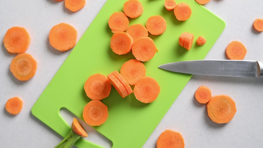 Young fresh carrots cut into circles on cutting board on kitchen table with knife top view. Cutting vegetables close-up cooking at home healthy eating, vegetarian diet food. Season of fresh vegetables Royalty-Free Stock Footage #1091970693
