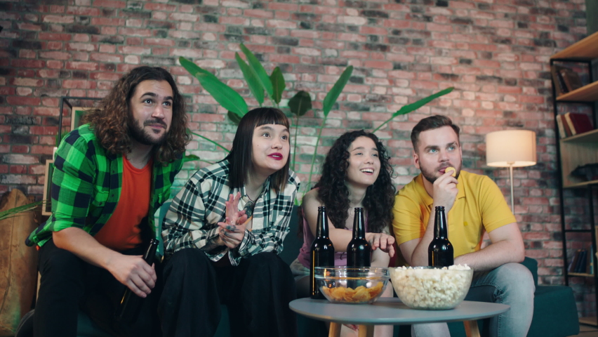 At some in living room concentrated group of friends watch football match happy and excited they celebrate the victory of the favourite team cheers with beers and eating some snacks | Shutterstock HD Video #1091976081