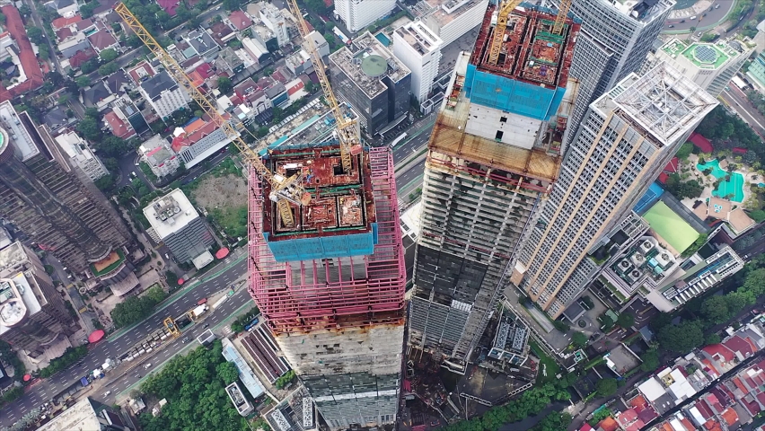 Close up aerial view of crane lowering an object on the roof of the skyscraper under construction in Jakarta, Indonesia | Shutterstock HD Video #1091979253