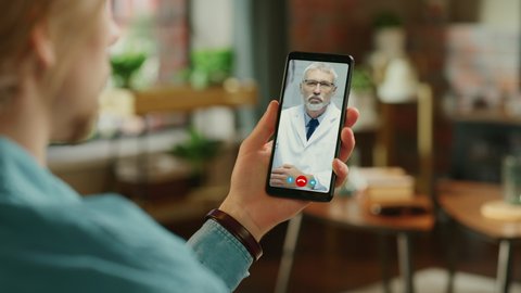 Young Man Sick at Home Using Smartphone to Talk to a Doctor via Conference Video Call on Medical App. Beautiful Woman Checks Possible Symptoms with Professional Physician, Using Online Video Chat