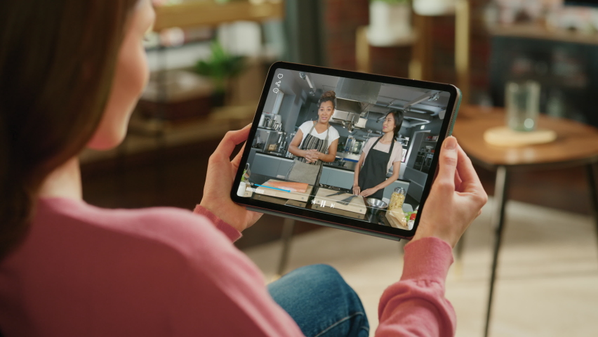Close-up Over the Shoulder. Woman Using Digital Tablet Computer, Watching Cooking Show Live Video on Demand Streaming Service, Two Professionals Chefs Preparing Delicious Dishes. Mock-up TV Show