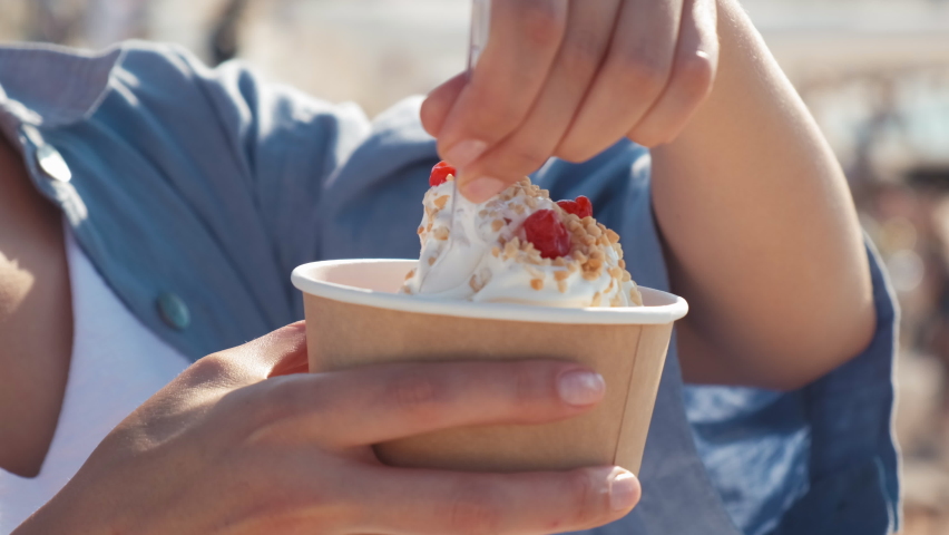 Close-up of a girl on the beach eating a newlywed. A woman eats yogurt ice cream with cherries and peanuts. a woman's hand takes ice cream with a spoon Royalty-Free Stock Footage #1091981675