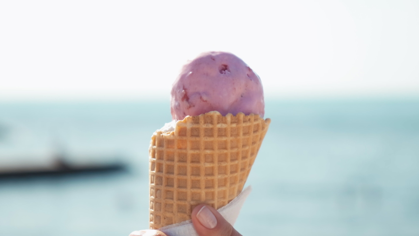 a girl eats ice cream in a cone on the beach. a girl goes with an ice cream cone on the beach. close-up of lips with strawberry ice cream