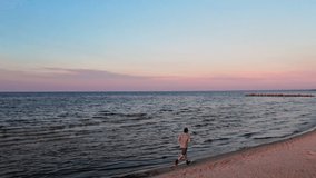 A young guy runs along the sea, he is engaged in sports jogging, the guy goes in for sports along the seashore at evening sunset, space for text, shooting from a drone
