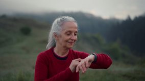 Senior woman jogger setting and looking at sports smartwatch, checking her performance in nature on early morning with fog and mountains in background. - Powered by Shutterstock - Get 15% off with code: PIKWIZARD15