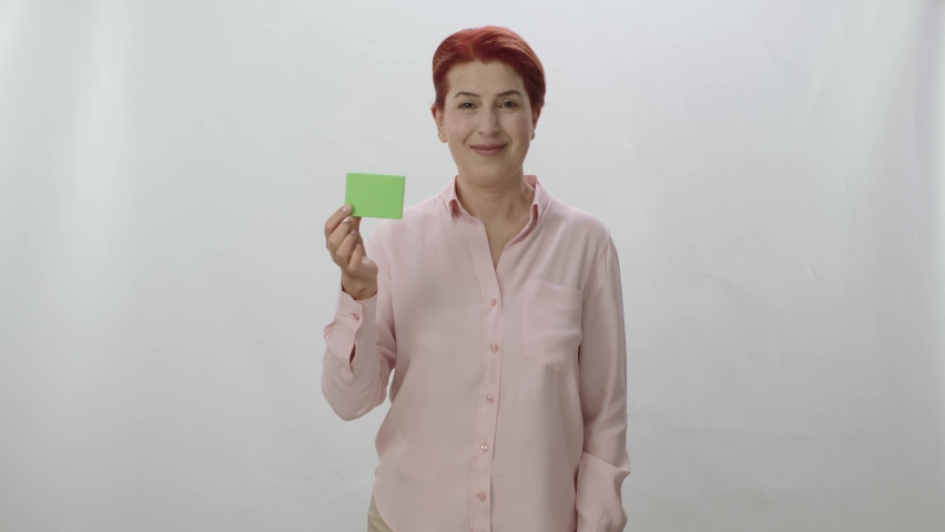 Studio portrait of a red-haired woman on a white background. Woman pointing at the product showing that the product is perfect. Creative 3d artists can replace the green box with any product they want