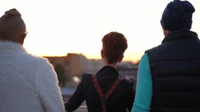 Back view relaxed Caucasian redhead woman standing with men on roof admiring urban city stretching hands. Carefree positive friends enjoying weekend evening resting on rooftop at sunset - Powered by Shutterstock - Get 15% off with code: PIKWIZARD15