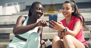 Female athletes laughing while looking at a funny video online together at a stadium. Sporty female friends and teammates enjoying using social media and searching internet at a sports ground