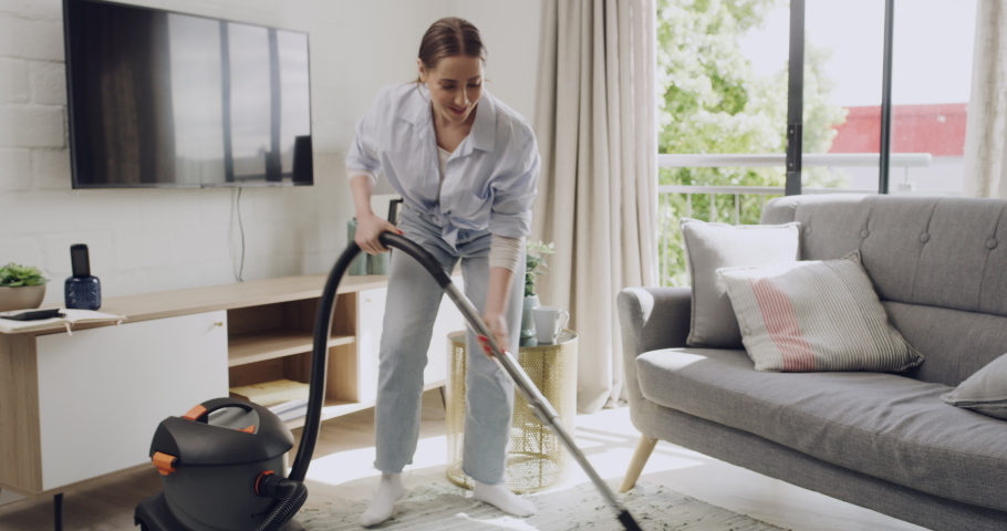 Young woman cleaning and dancing with vacuum cleaner in her apartment. Cheerful female listening to music while doing housework at home. Energetic female doing chores spring cleaning a lounge Royalty-Free Stock Footage #1091995835