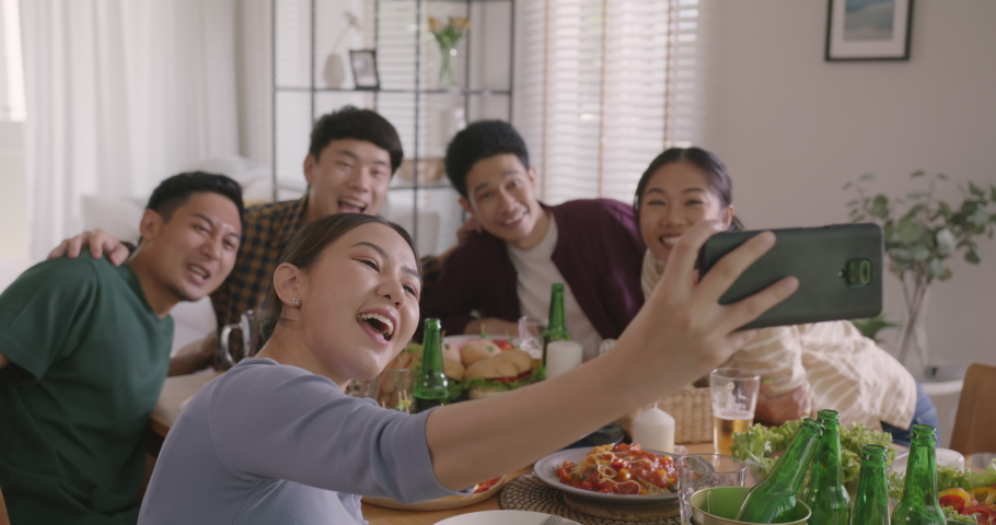 Happy hour diner at home relax smile look at camera shooting video photo on mobile app. Group of asia people young adult friend man and woman sit at dining table joy fun talk or eat food drink beer. | Shutterstock HD Video #1091997645