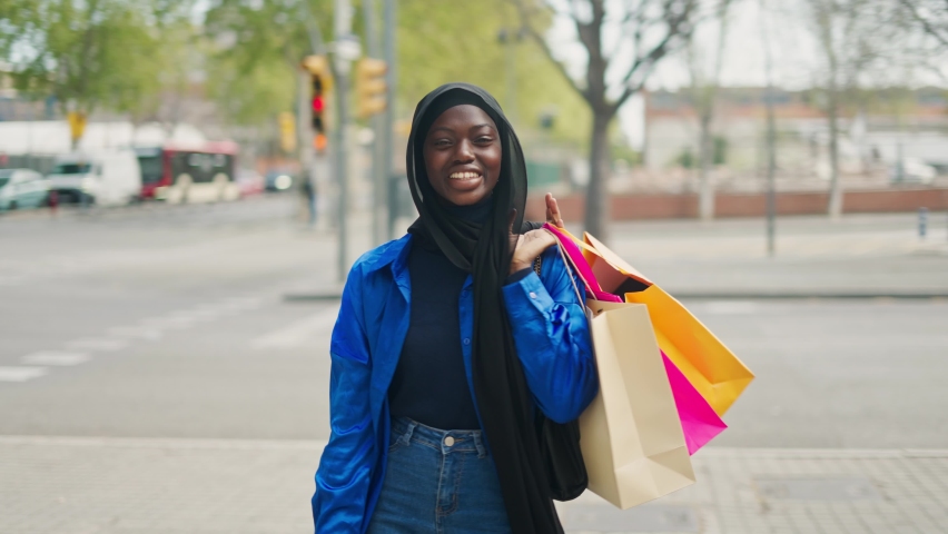 Positive Muslim shopaholic with paper bags on street