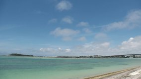 TOMIGUSUKU, OKINAWA, JAPAN - AUGUST 2021 : View of Senaga island beach (Ocean or sea) and airplane in daytime. Clear blue summer sky and clouds. Holiday, vacation and resort concept video.