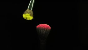 Makeup brushes touch each other on black dark background and small particles of color cosmetics, super slow motion, 1000 fps FullHd video