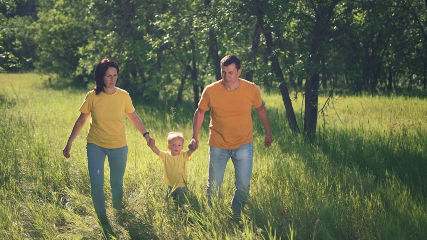 Happy family. Kid with dad and mom plays in the park. Parents with a child run on green grass in a forest park. Family picnic in the park on vacation. Green trees in the sun. People run holding hands
