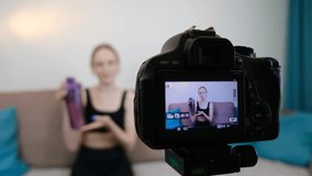 Camera close-up. A fitness blogger talks to the camera about a sports bottle. Blogger records video on camera at home. A young girl communicates on a video camera. Slow motion.