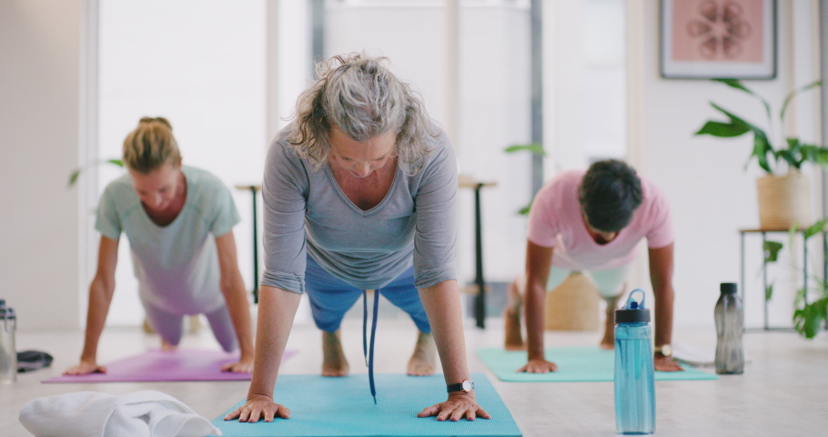 Active mature women bending in a downward facing dog pose during a fitness class in a yoga studio. Yogi training a group of calm and relaxed ladies. Exercising to improve health and wellbeing Royalty-Free Stock Footage #1092012885