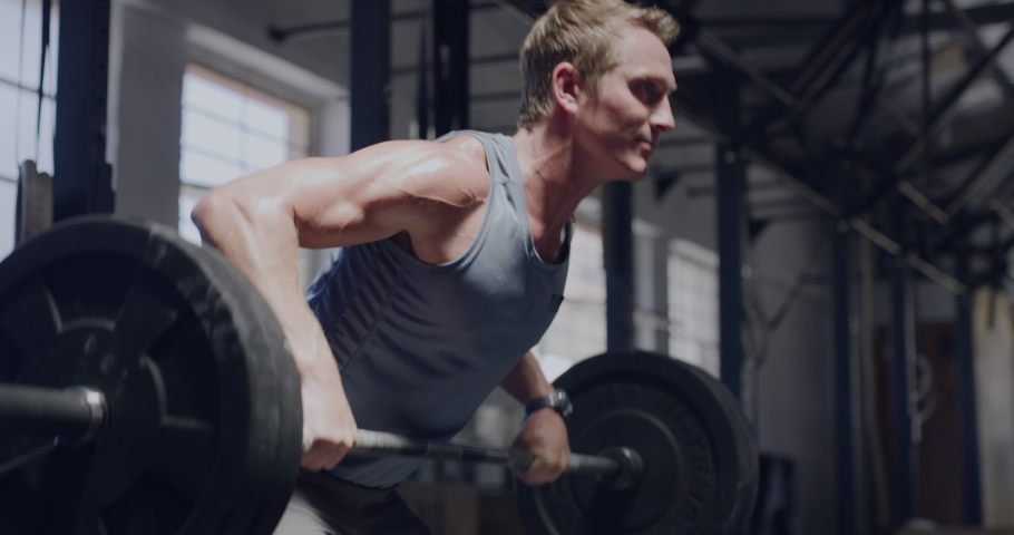 Muscular man lifting a barbell while doing bent over rows in a gym. Fit young bodybuilder staying focused while challenging himself by lifting heavy weights to gain muscle and endurance in a workout
