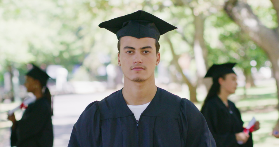 Portrait of a male university or college graduate standing outside and looking at the camera on graduation day. Proud young man in mortarboard and gown celebrating success in education and studies Royalty-Free Stock Footage #1092013067